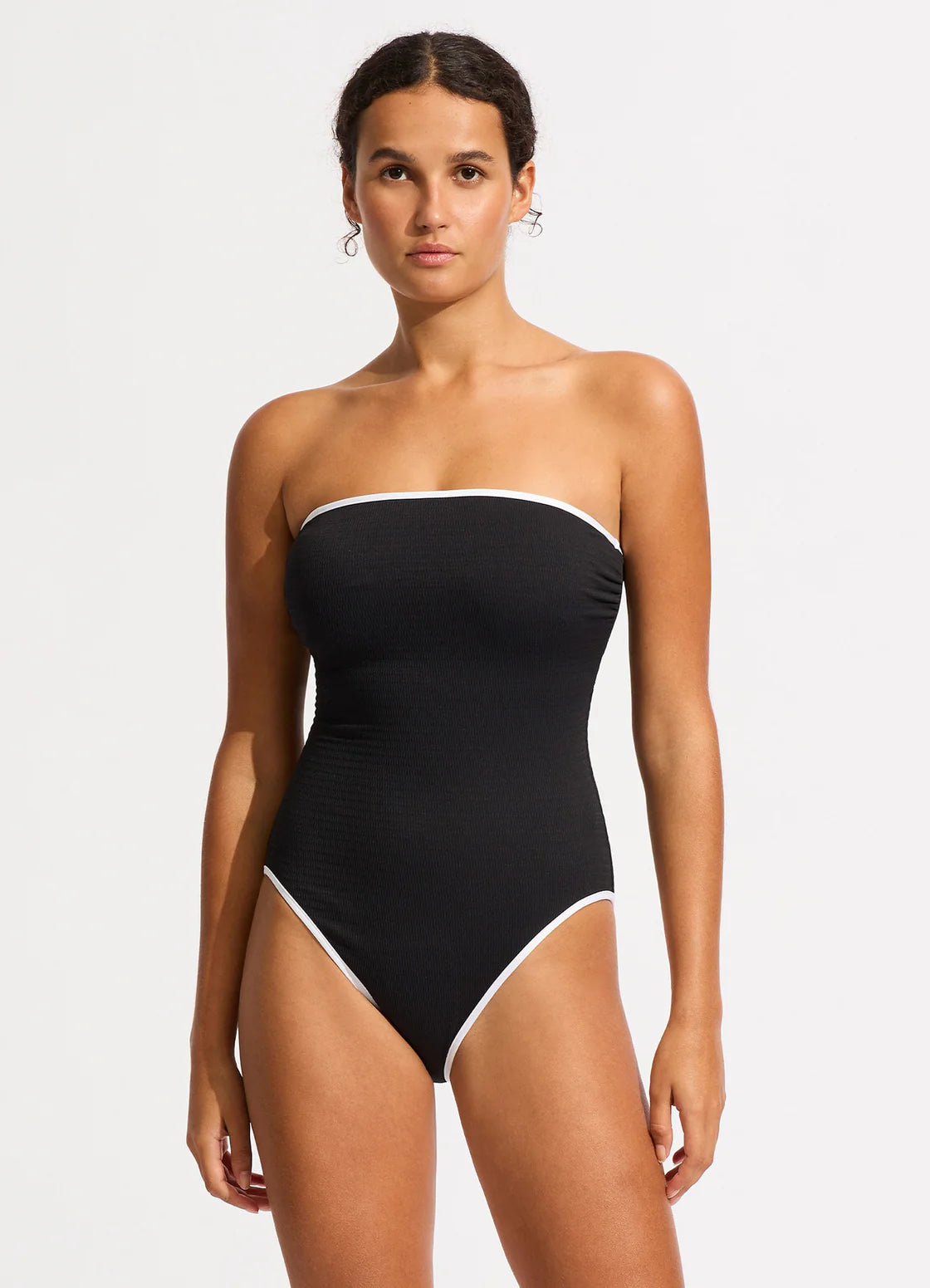 Woman wearing a black strapless swimsuit with white trim on a light gray background