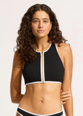 Woman wearing a black sports bra with a zipper on a plain background