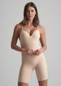 Woman wearing a beige bodysuit against a gray background