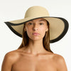 Woman wearing a wide-brimmed straw hat with black trim on a white background