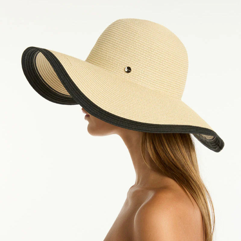 Beige sun hat with black brim worn by a person on a white background